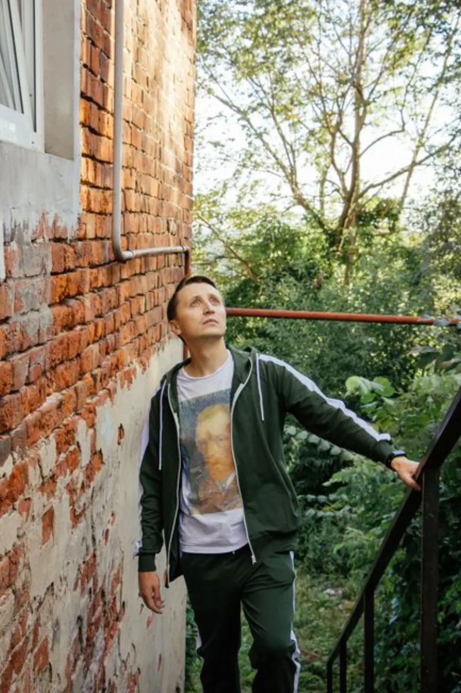 Man in a green tracksuit casually posing outside against a brick wall.