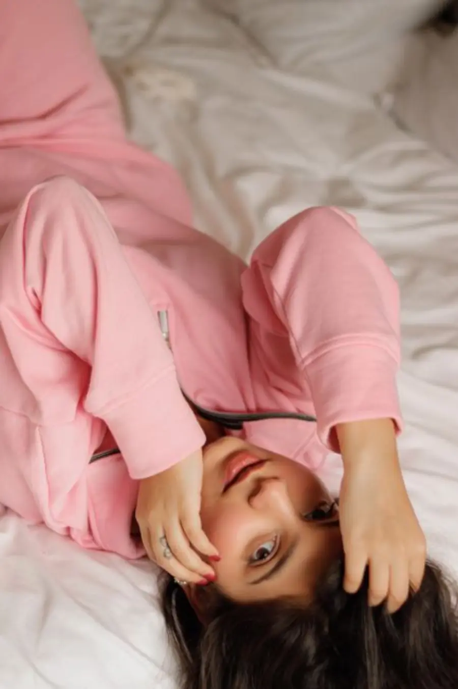 Young woman in a pink sweatsuit lying on a bed, looking comfortable and relaxed.
